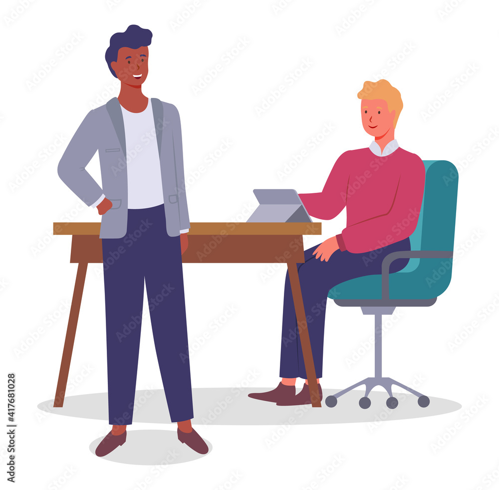 Two young office workers communicate, laugh. Guy with red sweater sitting on green chair at table with laptop. Man standing and talking. Informal friendly communication between office workers Two young office workers communicate, laugh. Guy with red sweater sitting on green chair at table with laptop. Man standing and talking. Informal friendly communication between office workers