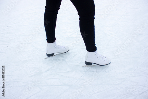 Close-up of female legs in white figure skates on an outdoor ice rink. Young woman skating on a skating rink in a snowy winter park