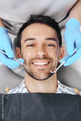 Smiling young man sitting in dentist chair while doctor examining his teeth