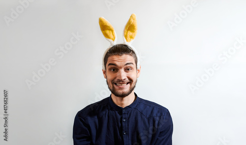 Man with rabbit ears. Charming young man with beard in shirt wearing Easter bunny costume. Persom with hare ears smiles big smile. Creative banner for celebration of Easter. photo