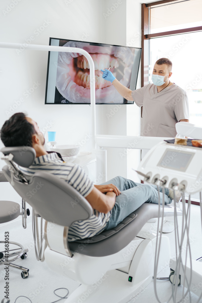 Obraz premium Dentist discussing with laying patient showing the image of his teeth on the screen