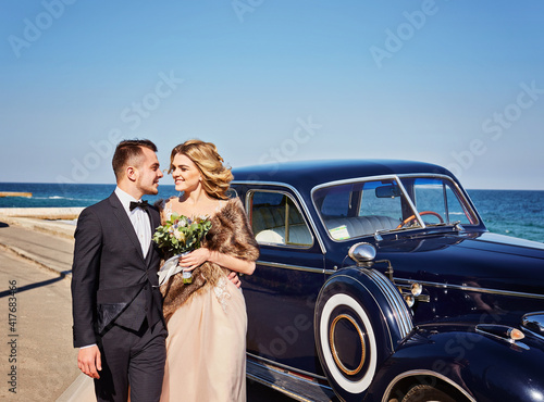 Happy bride and groom hugging and posing near old retro car