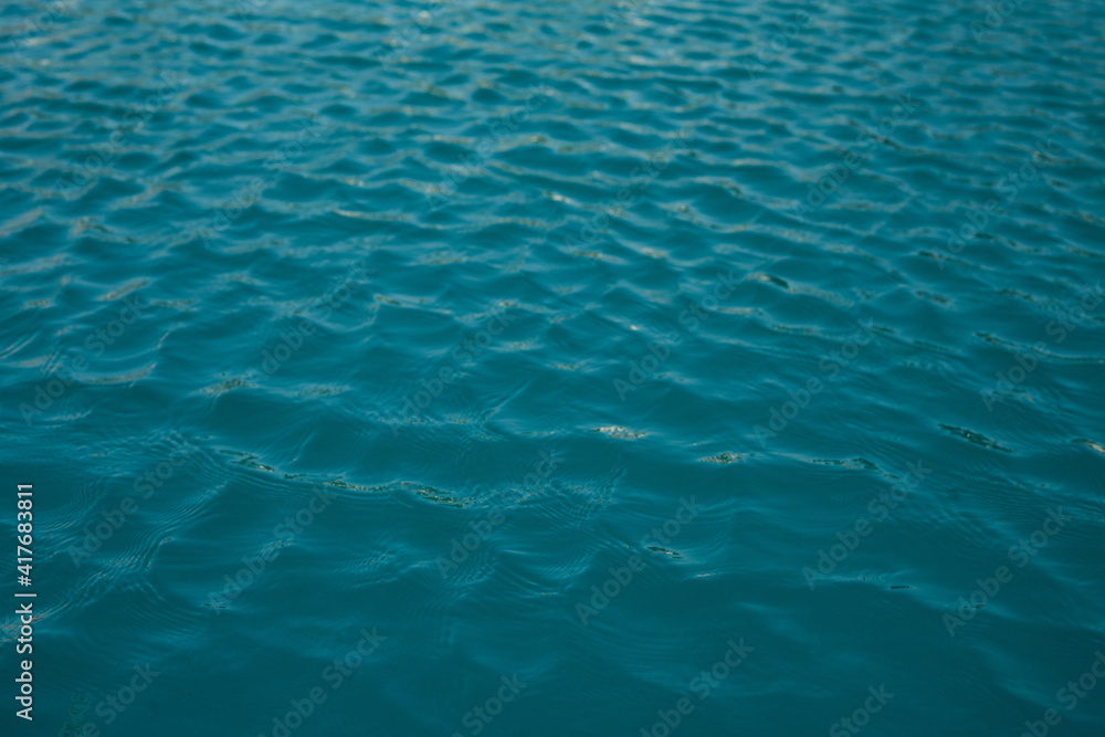 The texture of clear blue water with small waves on a sunny day. Peace and tranquility. Background The texture of clear blue water with small waves on a sunny day. Peace and tranquility. Background