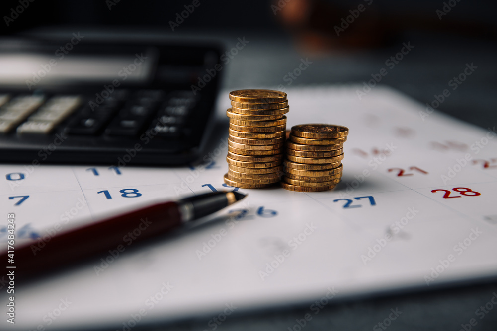 Calendar, calculator and stack of coins in a office. - obrazy, fototapety, plakaty 