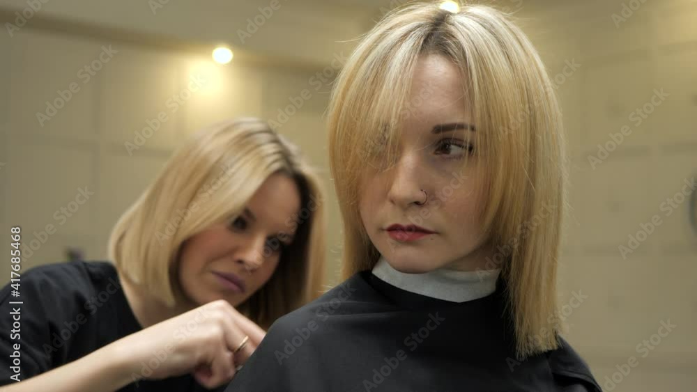 Hairdresser is making haircut to the client woman. Blonde women. Indoors in the beauty salon, barber shop. Hairdresser is making haircut to the client woman. Blonde women. Indoors in the beauty salon, barber shop.