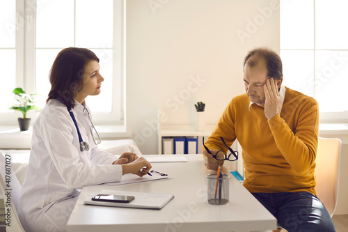 Tired senior man telling doctor about pains and severe headaches. Physician listening to male patient complaining about migraine  high blood pressure  stress  fatigue and weakness