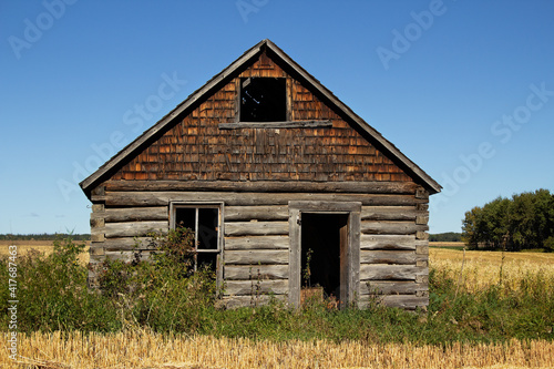 The front of an abandoned gray weathered log cabin in good shape in a field in a countryside landscape