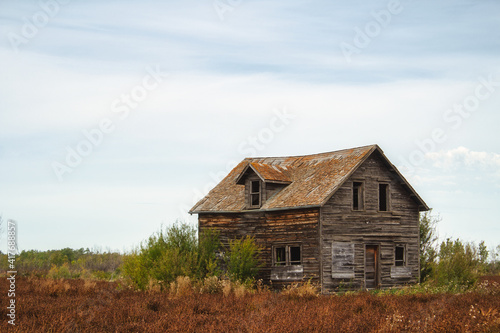 A beautiful wooden weathered two story old farm house dotted with green shrubs under a sunny sky in a countryside landscape