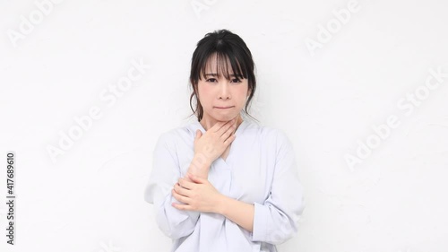 白い壁の前に立って喉が痛いジェスチャーをする若い女性