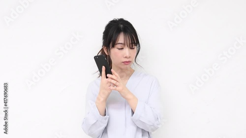 白い壁の前に立ってスマホを使う若い女性