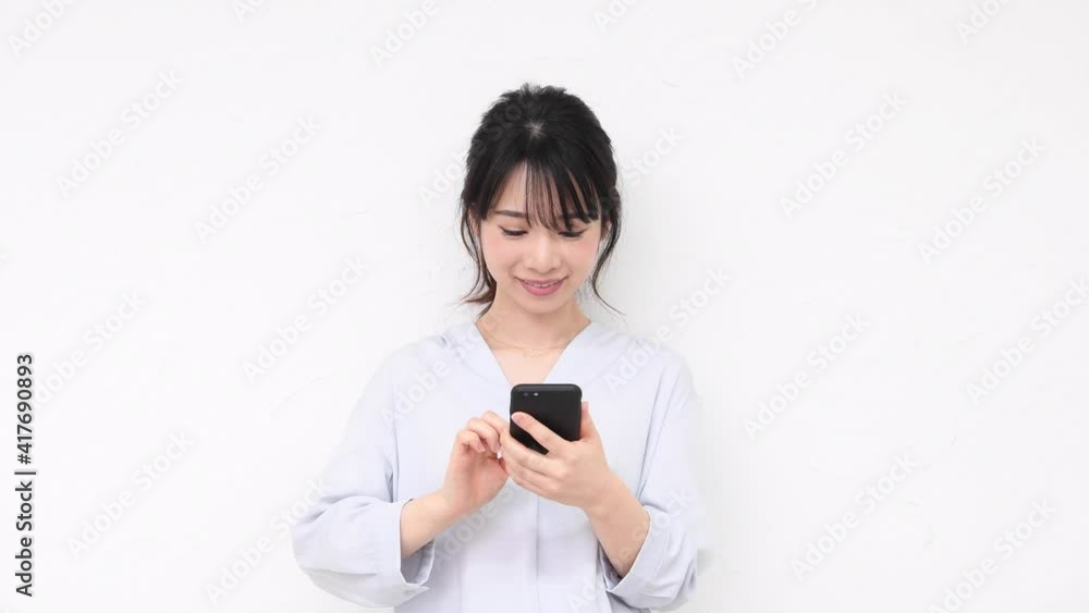 白い壁の前に立ってスマホを使う若い女性 白い壁の前に立ってスマホを使う若い女性