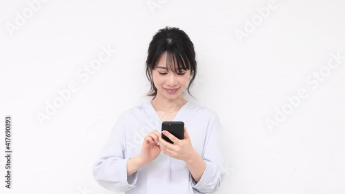 白い壁の前に立ってスマホを使う若い女性