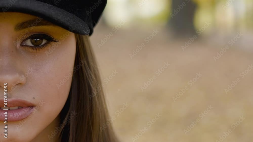Girl looking into camera on autumn background. Maple leaf passing over her face Girl looking into camera on autumn background. Maple leaf passing over her face