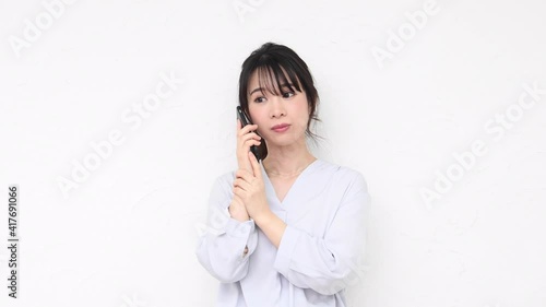白い壁の前に立ってスマホを使う若い女性