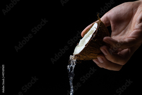 Isolated coconut on a black background. Coconut milk is poured from half a coconut. Half of a coconut in a man's hand on a dark background. Healthy fruit
