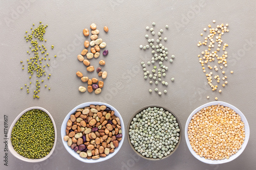 Different types of legumes in bowls and scattered in the background, green and yellow peas, mung beans and brown beans, top view © pundapanda