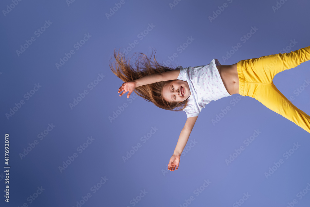 crazy excited little fun girl hanging happy upside down hands up on isolated purple studio background. Dynamic children's image. Emotions, expression. Copy space crazy excited little fun girl hanging happy upside down hands up on isolated purple studio background. Dynamic children's image. Emotions, expression. Copy space
