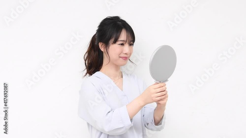 白い壁の前に立って鏡を見る若い女性
