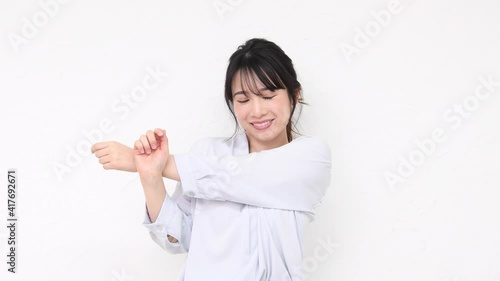白い壁の前に立ってストレッチをする若い女性