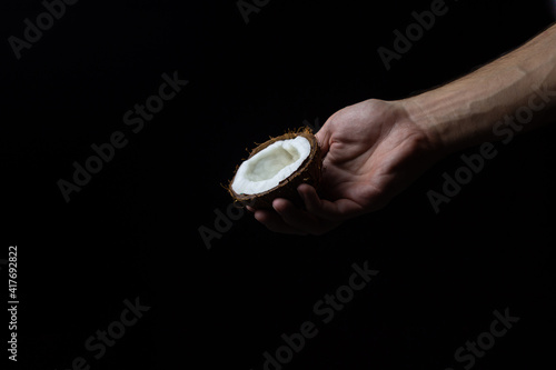 Isolated coconut on a black background. Half of a coconut in a man's hand on a dark background. Healthy fruit