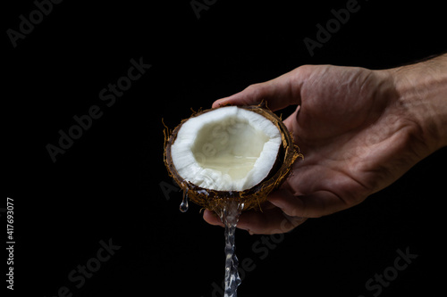 Isolated coconut on a black background. Coconut milk is poured from half a coconut. Half of a coconut in a man's hand on a dark background. Healthy fruit