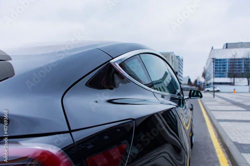 Black modern electro car on the background of the road. Car backside view.
