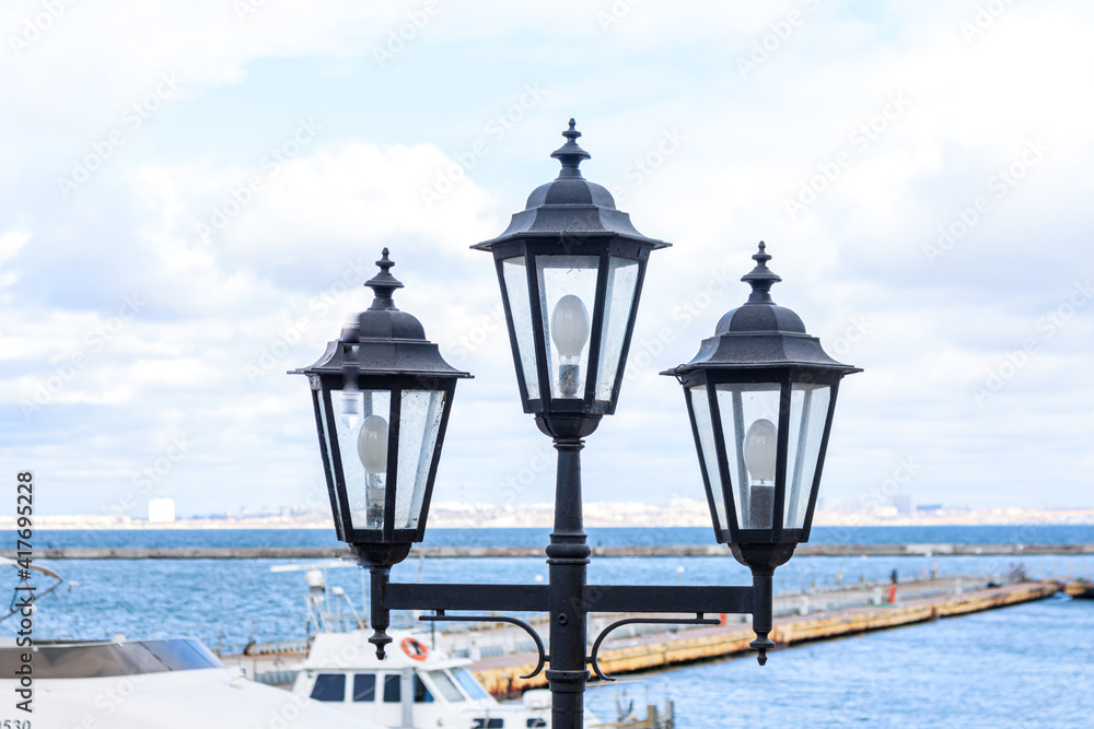 Odessa, UKRAINE - MART 1, 2021. Lantern to illuminate the sea pier in the port of Odessa. Odessa port, Ukraine. A booster boat stands in the background of the lantern.