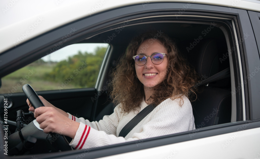 Young woman smiling while holding the steering wheel of the car with her hands.