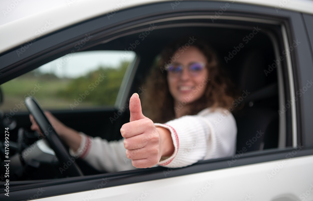 Young woman driving making a thumbs up gesture with her hand. New driver concept