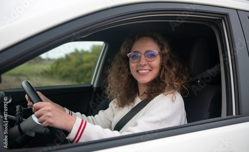 Young woman smiling while holding the steering wheel of the car with her hands. © Clipfy