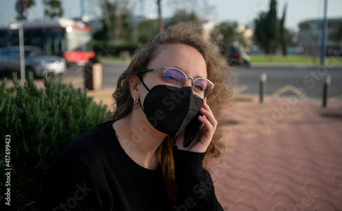 Young woman with mask talking on the phone in street. Covid 19 or coronavirus.