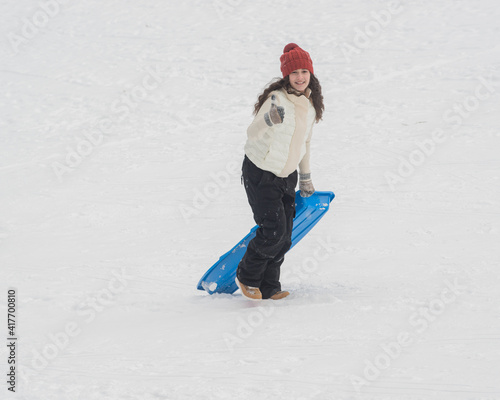 Girl carrying sled up hill giving thumbs up sign
