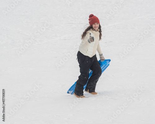 Girl carrying sled up hill with thumbs up sign