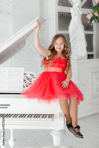 Beautiful little girl in pink dress sitting on a chair and playing the piano. Cute girl in a fluffy dress at the piano on a light background