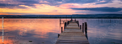 Amazing mood sunset at a lake coast with a boat at a wooden pier. Panoramic view