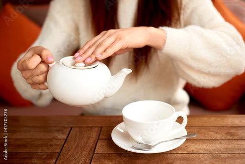 female hands pouring tea from teapot into a white cup on wooden table