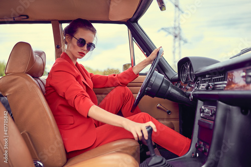 Beautiful young woman wearing red costume and sunglasses sitting in retro car © zamuruev