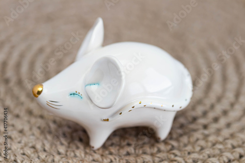 Porcelain figurine of a white rat on a background of wicker straw or jute.