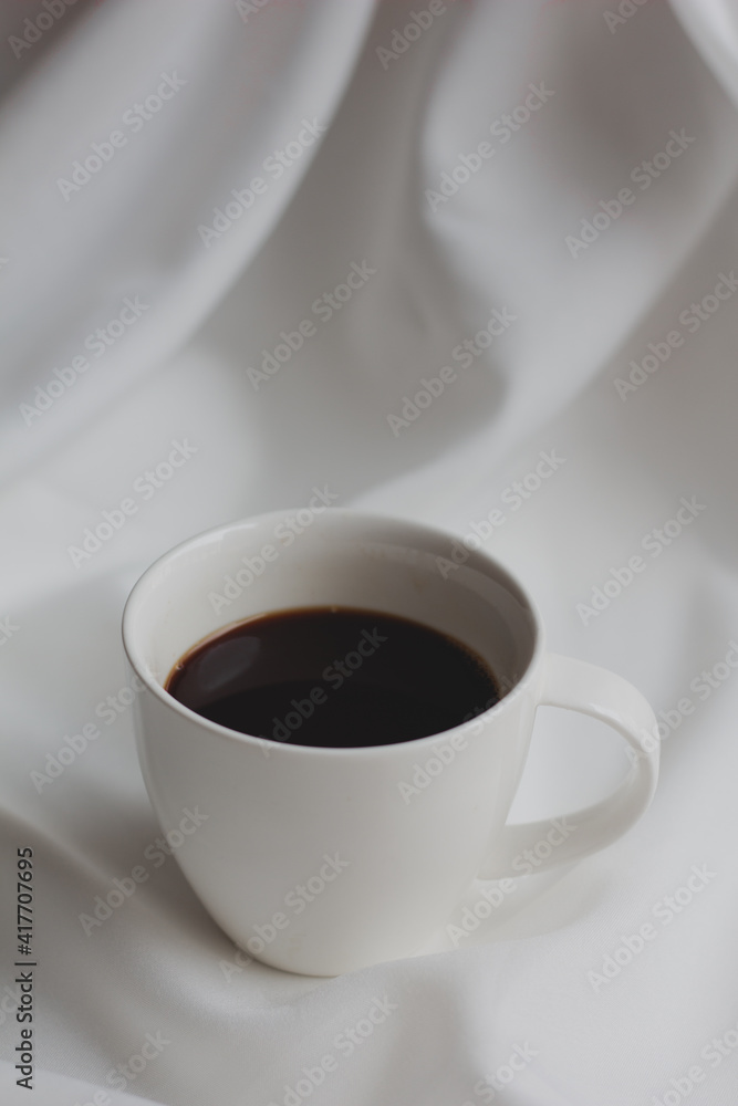 Cup of hot coffee on a white fabric layer with soft light and shadow in the morning, minimal, retro. Cup of hot coffee on a white fabric layer with soft light and shadow in the morning, minimal, retro.