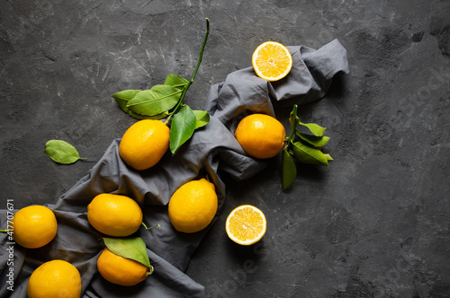 Fresh ripe yellow lemon fruits with leaves on dark stone background