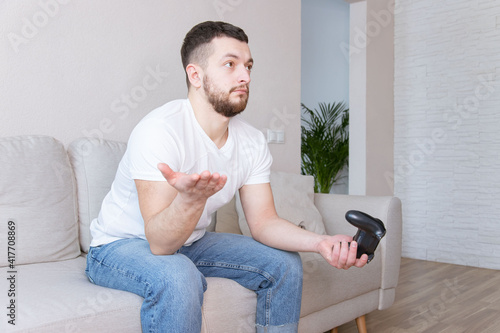 Angry man playing video games at home. People emotions lifestyle concept. Play game with joystick spreading hands.