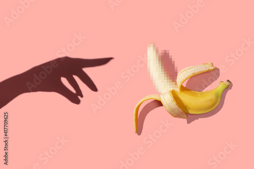 Принти на полотні Symbol of the penis in the form of a ripe banana with blurred censored squares and female hand on a pink background, place for text