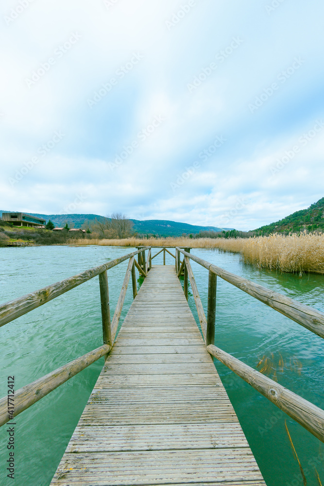 fishing gangway with walkway entering the water with green tones and blue sky with clouds in idyllic setting