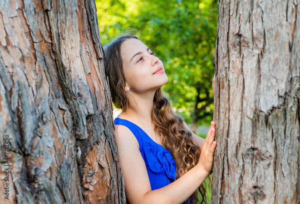 Little kid dreamer with long wavy hair and beauty look dream at tree trunk in summer park, future Little kid dreamer with long wavy hair and beauty look dream at tree trunk in summer park, future