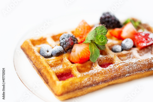 Fried waffle sprinkled with powdered sugar with pieces fresh fruits and berries
