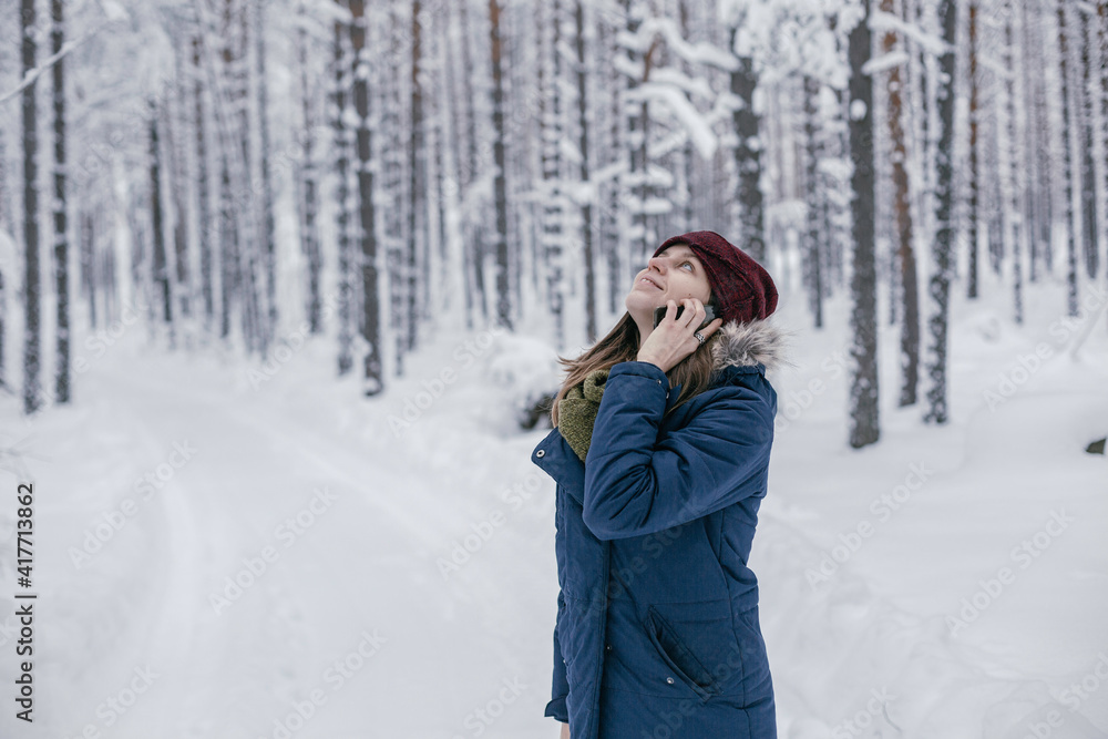 Beautiful girl calls a taxi in the winter forest