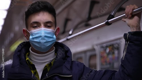 Closeup of masked teen boy dressed in autumn jacket having trip on subway during covid-19 infection outbreak. Law abiding brunette teenager wearing medical face mask while riding in underground