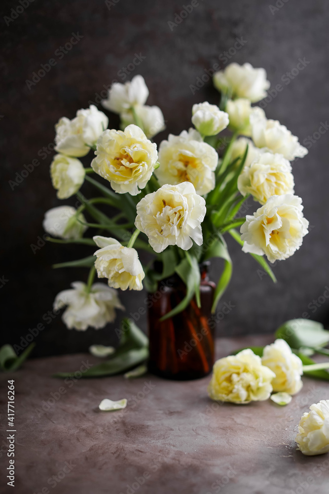 Beautiful yellow tulips in a glass dark vase on a gray background. Festive bouquet. Flower decoration for the home.