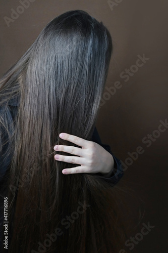 young long haired brunette unraveling combing her hair with a wooden brush with natural bristles on dark brown background, concept of hygiene, hair care