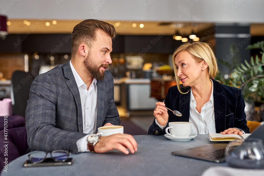 middle-aged man and woman discussing projects using laptop, at business meeting, in formal wear